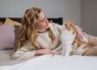 A woman lovingly holds a fluffy cat on a bed