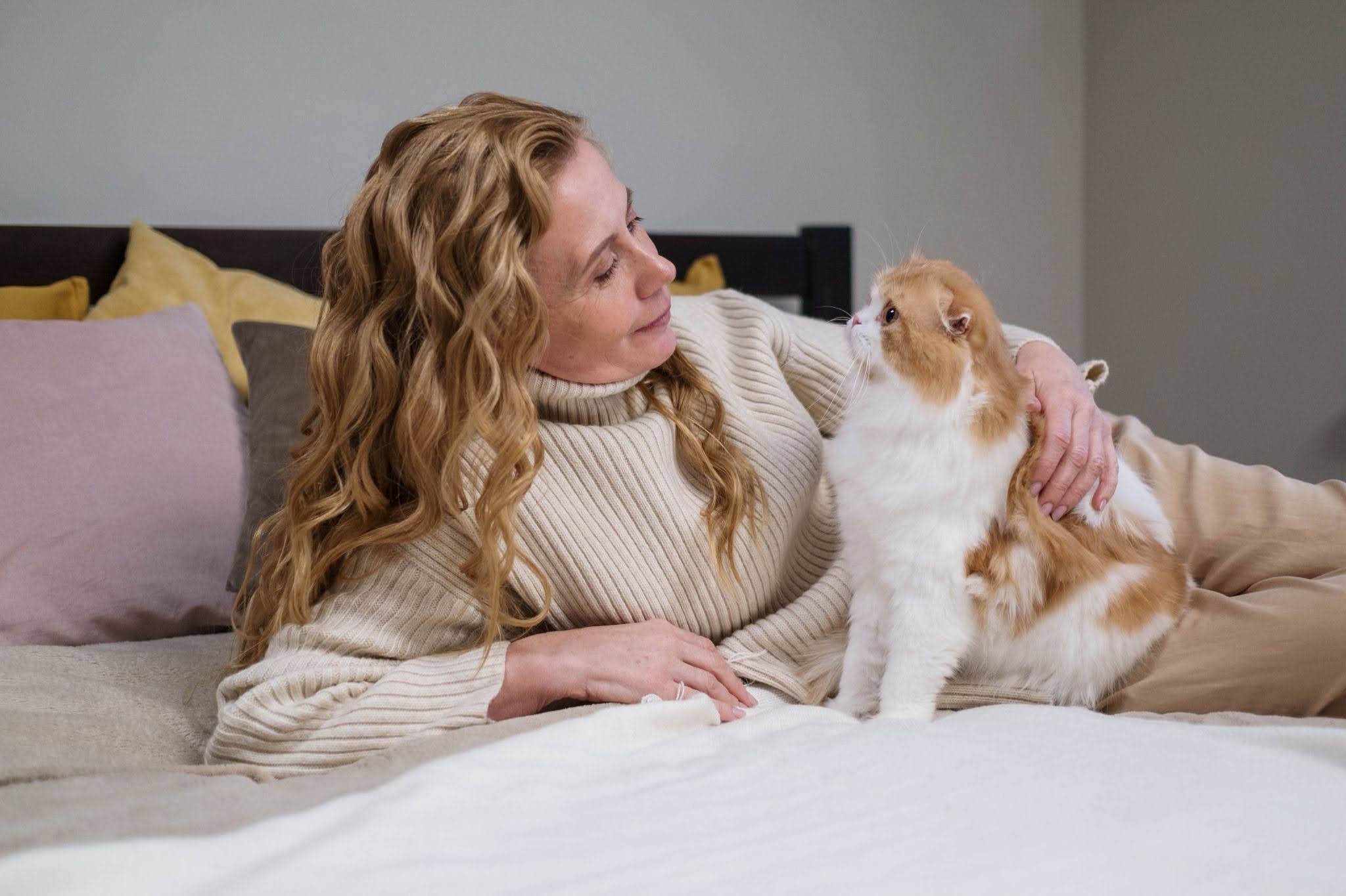 A woman lovingly holds a fluffy cat on a bed